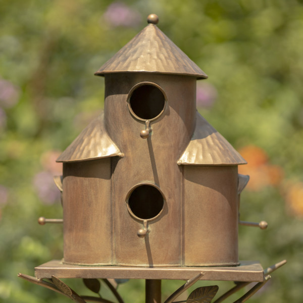 Close up image of Copper triple cylinder conical roof birdhouse stake with vines and leaves running under the bottom rim of the birdhouse holding it up and there are circular holes on the birdhouse for birds to enter