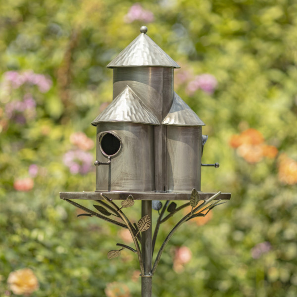 Side back view image of Antique silver triple cylinder conical roof birdhouse stake with vines and leaves running under the bottom rim of the birdhouse holding it up and there are circular holes on the birdhouse for birds to enter