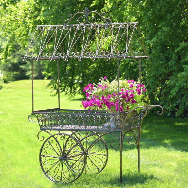 Large iron flower cart with 2 moving wheels holding bright pink flowers in antique style painted in distressed bronze finish