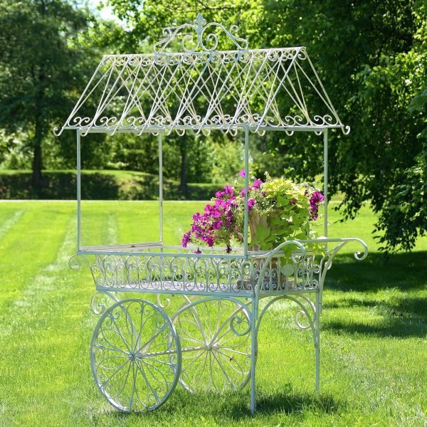 Large iron flower cart with 2 moving wheels holding bright pink flowers in antique style painted in distressed white finish