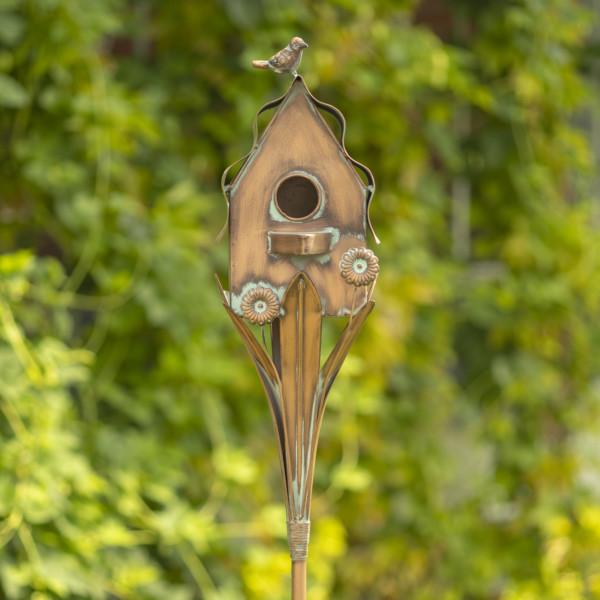 Close up image of Tall cotton style birdhouse garden stake with small bird sitting at the top of the roof and leaves holding up the birdhouse