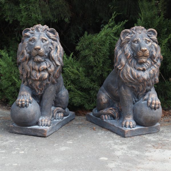 Set of 2 26.5 inches tall magnesium lion sentry statues with stone-like appearance in antique bronze finish with a ball under a paw Marloni and Antonio in a garden