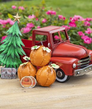 small vintage red iron pickup truck with three pumpkins, Christmas tree and seasonal decimals in front of it