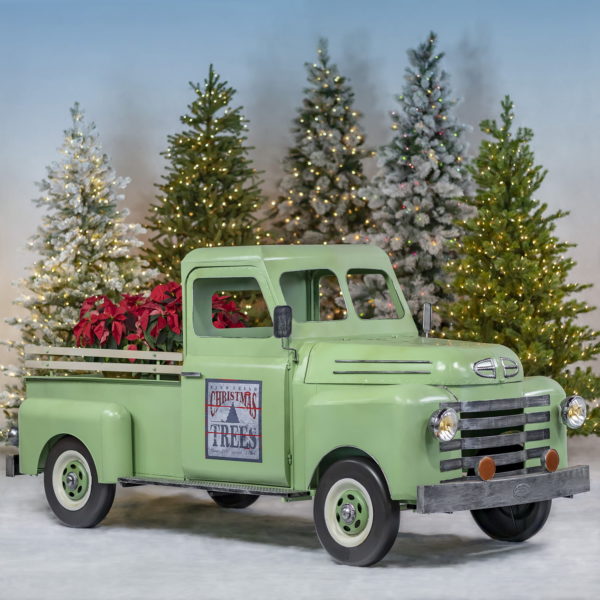 Life-size iron pickup truck in soft green with decimal on a passenger door and red Christmas plants in trunk