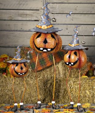 3 long legged jack-o-lantern pumpkins wearing witch hat Halloween figurines in front of haystacks