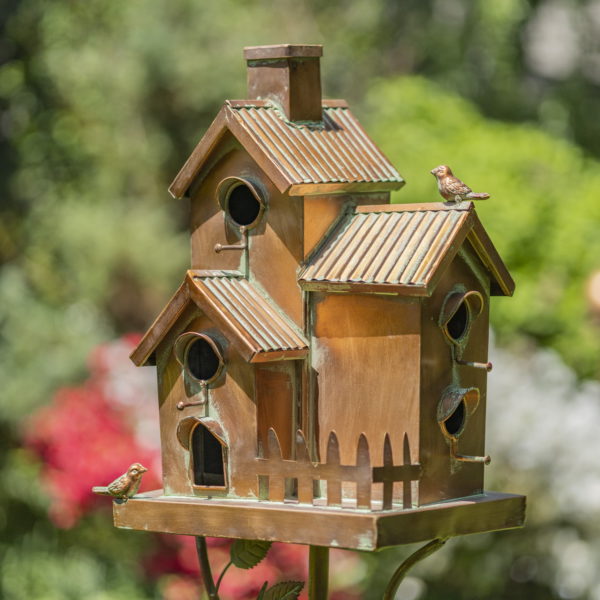 metal condo birdhouse with fence, chimney and two little birds perched on it painted in antique copper finish with patina details on a stake