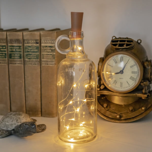 Bottle cork LED string lights inside clear wine bottle between old books turtle and diving helmet clock
