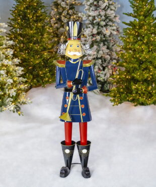 Life-sized iron Christmas blue nutcracker Harold holding trumpet in front of lighted up Christmas trees