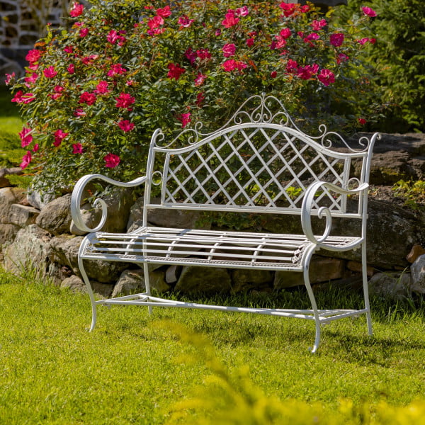 Side view of Victorian style iron garden bench in antique white distressed finish with exquisite lattice backrest with filigree details juxtaposed with the perpendicular slats of the seat in garden