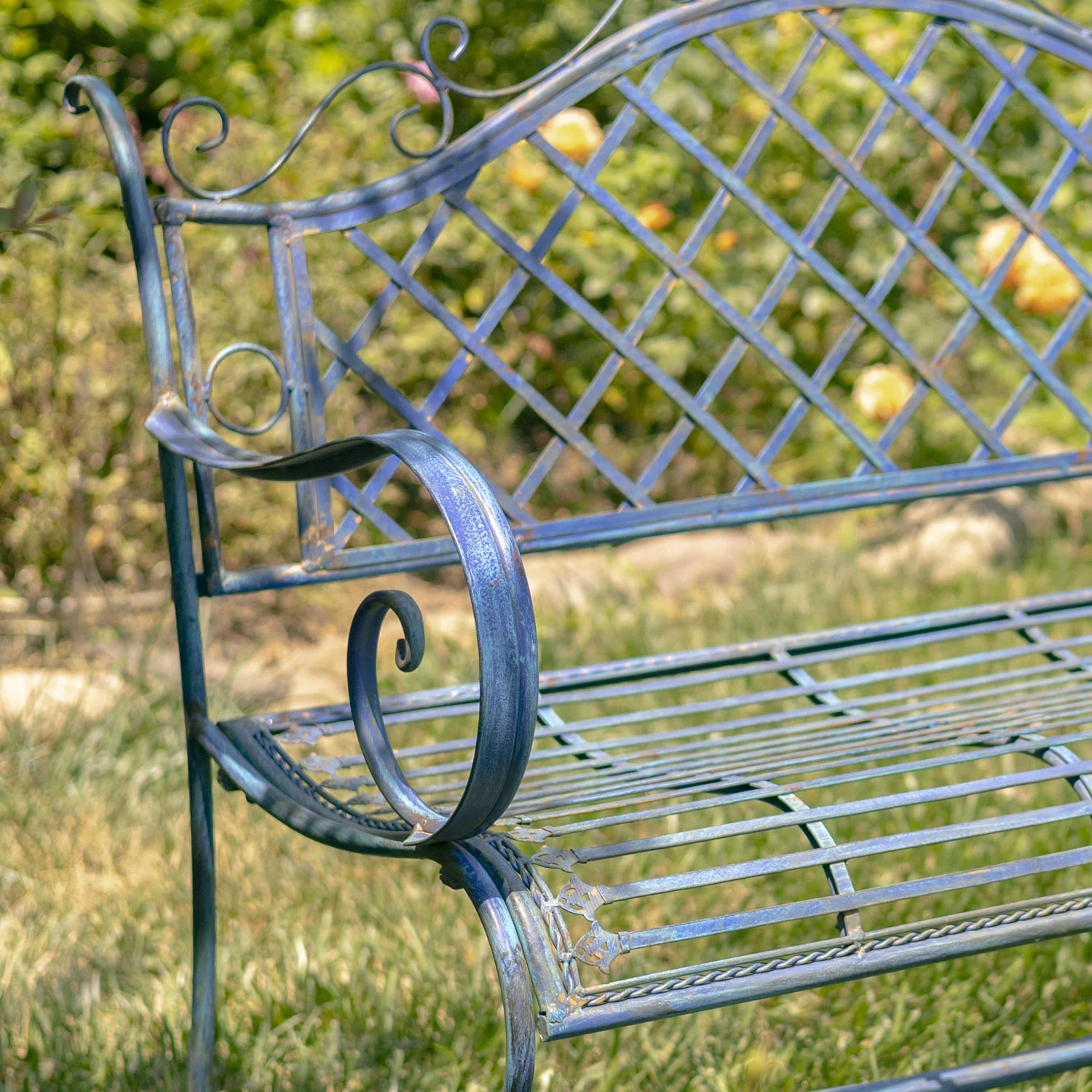 close up right side of Victorian style iron garden bench in antique blue distressed finish with exquisite lattice backrest with filigree details juxtaposed with the perpendicular slats of the seat in garden