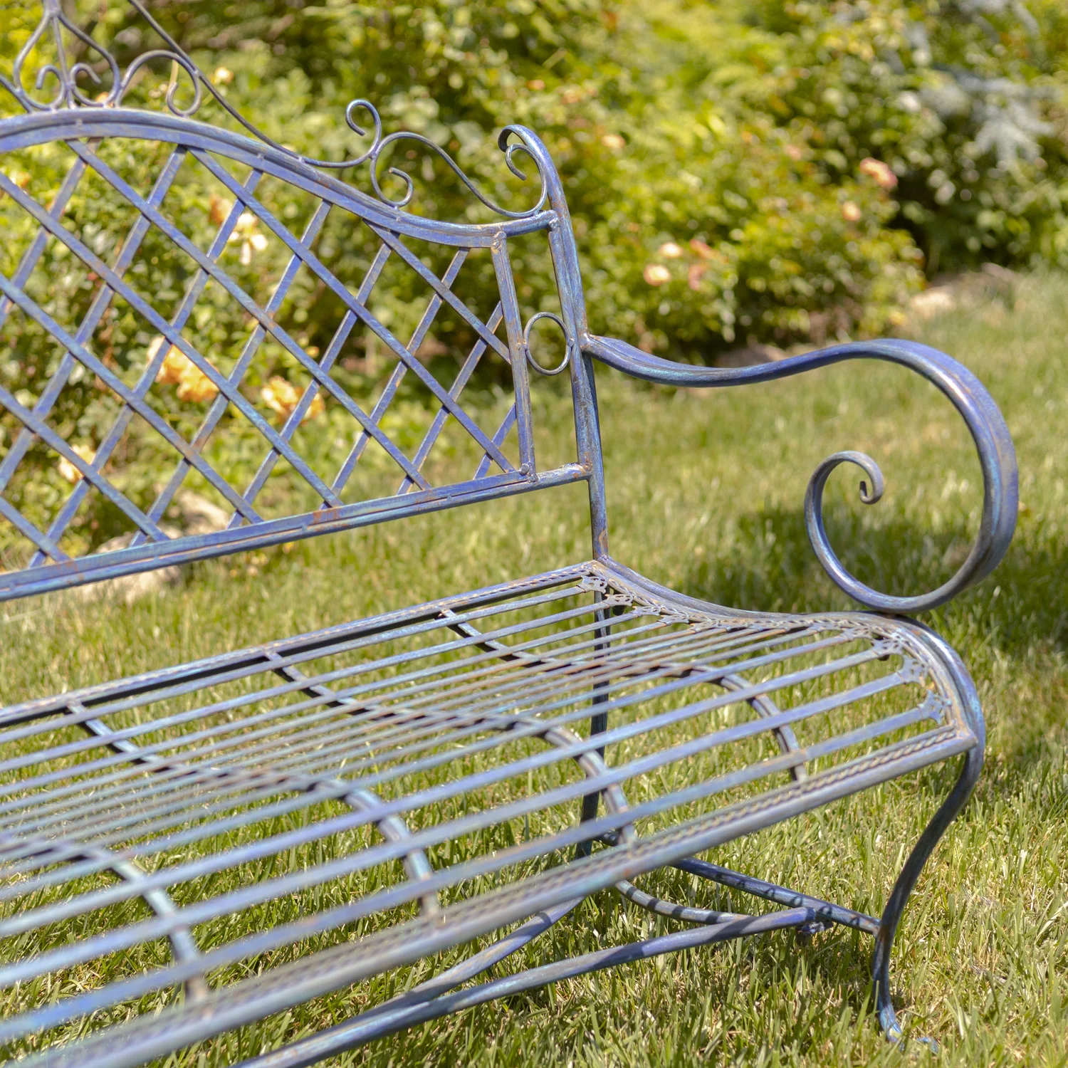 close up Victorian style iron garden bench in antique blue distressed finish with exquisite lattice backrest with filigree details juxtaposed with the perpendicular slats of the seat in garden