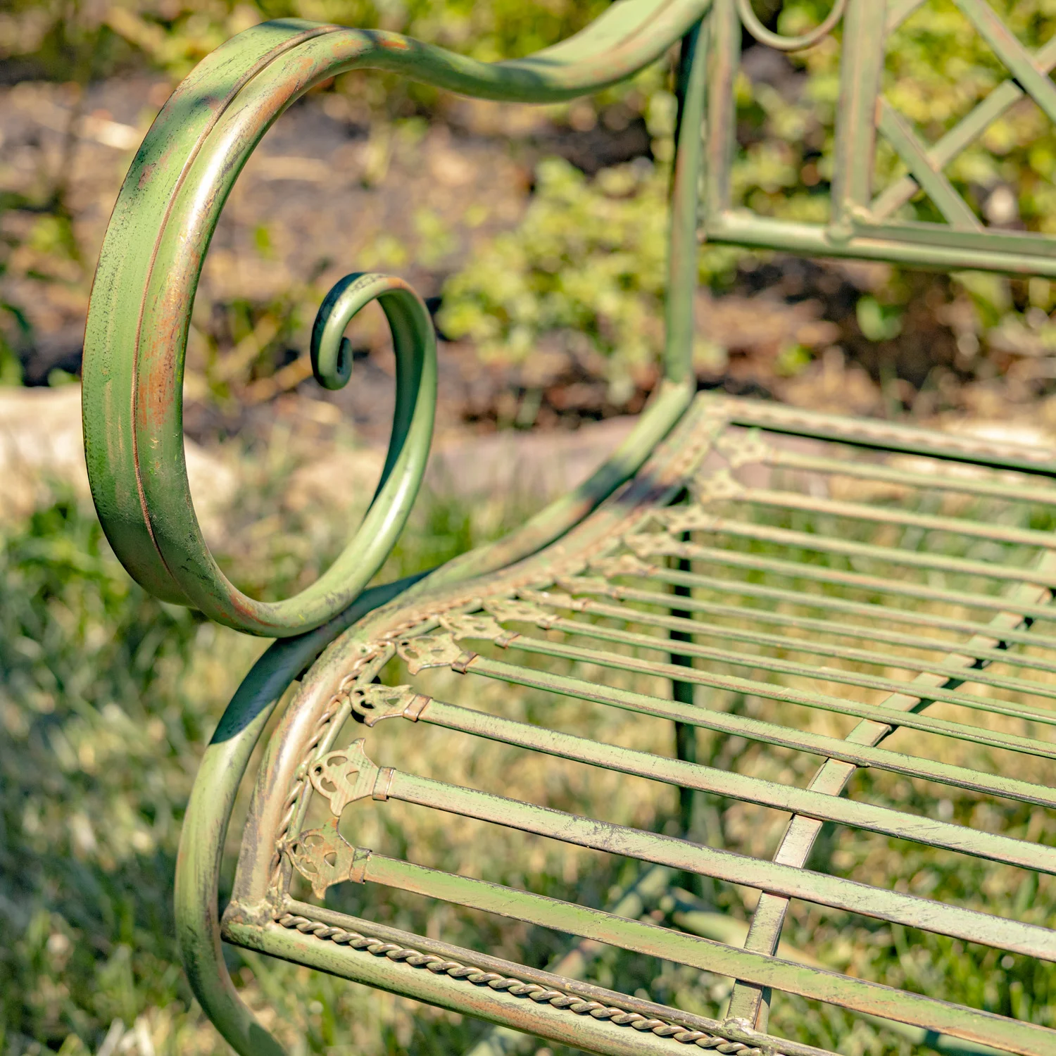 close up Victorian style iron garden bench in antique green distressed finish with filigree details juxtaposed with the perpendicular slats of the seat