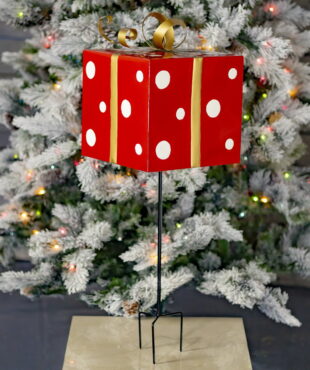32 inch tall red and white polka dot pattern metal Christmas gift box three prong yard stake with metallic gold ribbon in front of light-up tree