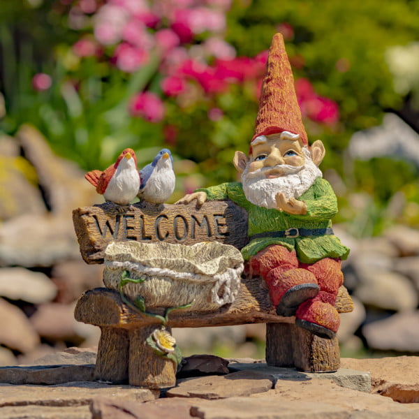 Spring garden gnome sitting on a bench with welcome sign birdbath and birds