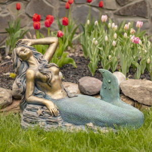 beautiful mermaid statue laying on rocks in tulip garden
