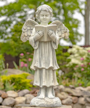 Antique white angel statue child standing in a garden reading a book with her wings speaded out