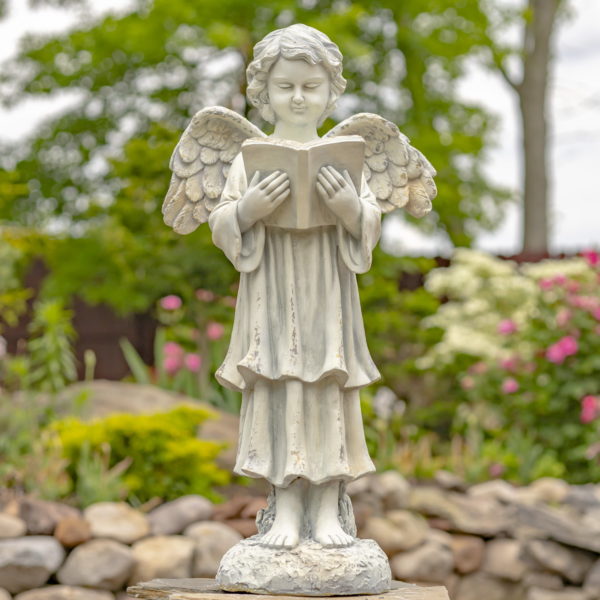 Antique white angel statue child standing in a garden reading a book with her wings speaded out