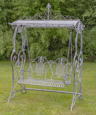 A large iron swing bench in blue bronze with curlicue designs on both ends of the swings , the backrest also has a curlicue design as well as the the top of the sheltered roof on the swing bench