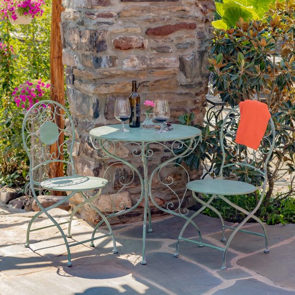 Antique green metal bistro set that includes two chairs and a table with curlicue designs, with wine bottle and 2 glasses standing on the table