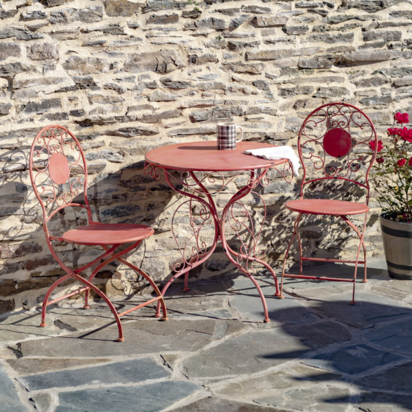 Flamingo pink metal bistro set that includes two chairs and a table with curlicue designs