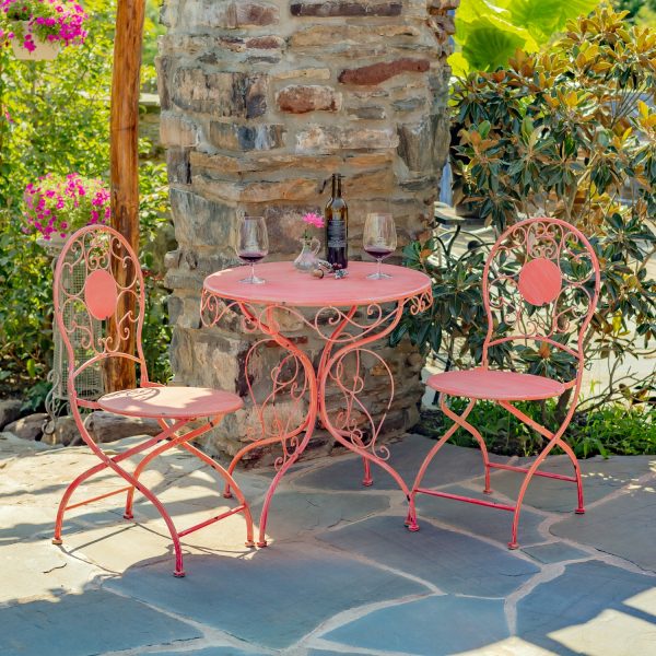 Flamingo Pink metal bistro set that includes two chairs and a table with curlicue designs, with wine bottle and 2 glasses standing on the table