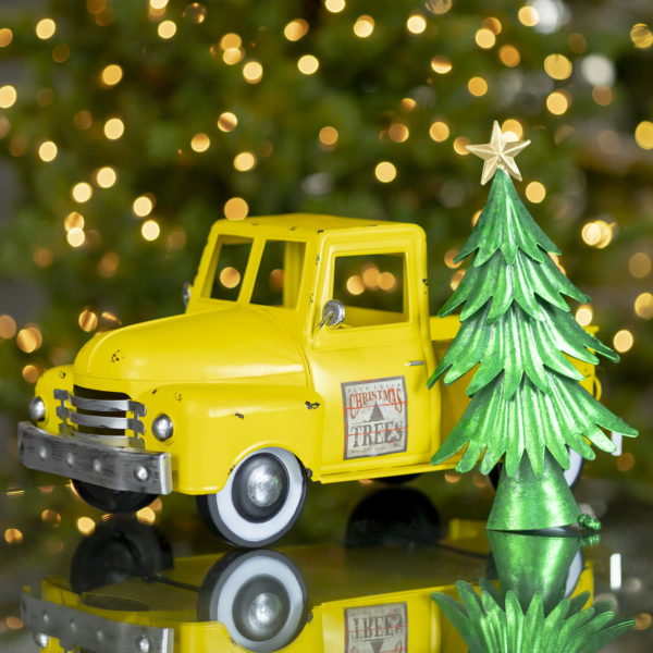 Small iron Christmas old style truck with decimal on a door next to tree in antique yellow finish
