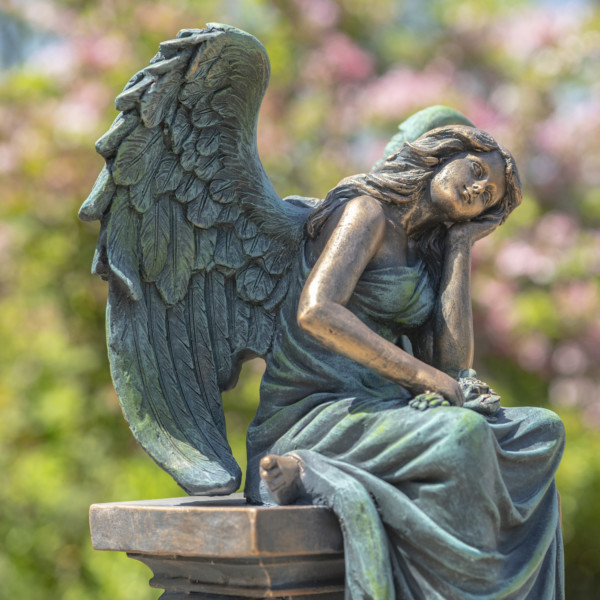 Green and bronze magnesium angel statue sitting on pillar with head rested on hand