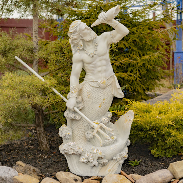 Tall antique grey merman garden statue holding a seashell spyglass in one hand and in the other holding a trident with his long hair and muscular body
