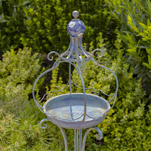Close up image of Tall standing blue iron birdbath with blue ceramic floral designed ball