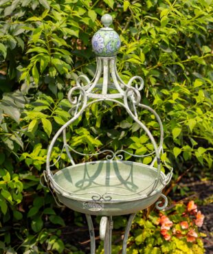 Close up image of Tall standing green iron birdbath with green ceramic floral designed ball