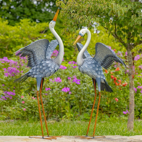 One set of two blue heron iron garden figurine with one standing tall with his head looking upright while the other one is looking downwards with his head slightly bent while their wings are standing up in the air