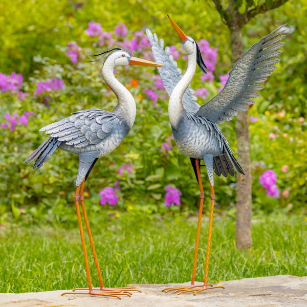 Set of 2 blue and white Iron Heron Garden Figurines with one standing tall looking up in the air with his wings spread wide open while the other one is standing beside him with his wings closed down just watching straight ahead