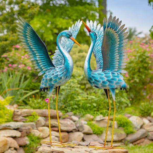 One set of Set of 2 Stylized Metallic Blue-Green Crane Garden Figurines standing tall with there both wings widely open up in the air with one slightly looking up while the other one is slightly looking down