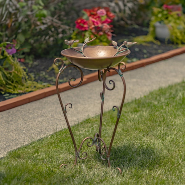 medium metal birdbath in antique copper finish with birds and tree branch on bowl and ornate stand in garden