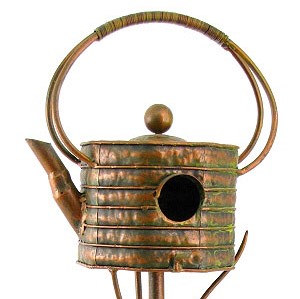 closeup of only the teapot shaped birdhouse with ribbed texture, large half circle handle with decorative grip in an antique copper finish against a white background