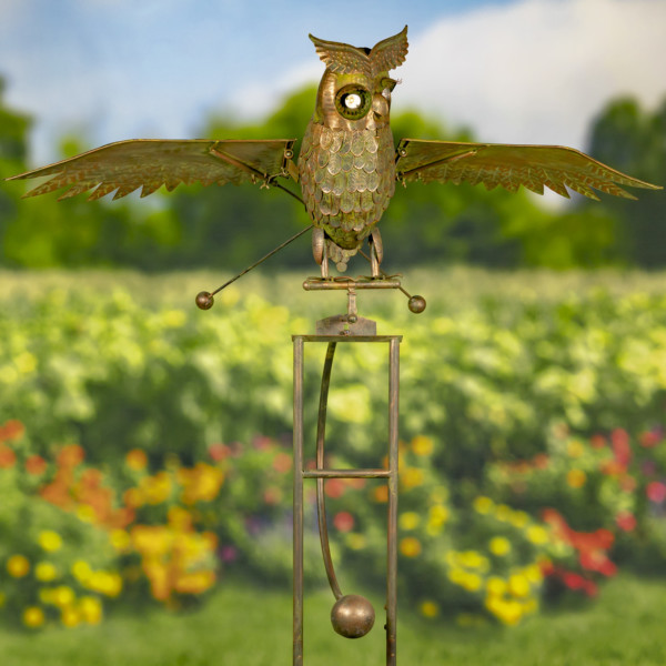 Close up image of bronze large solar metal flying Owl with large round eyes that lights up in the dark standing on a stake flapping his wings