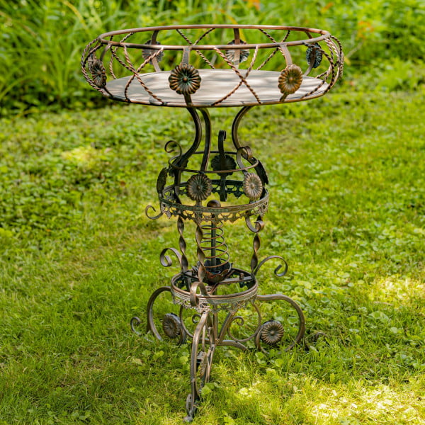 Iron round Victorian style planter table featuring aster blossom and rope-like twisted metal pattern in antique bronze distressed finish in garden