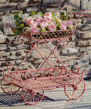 Flamingo red two tier flower push cart with four moving wheels and curlicue designs with pink flowers in it ( Flowers not included)