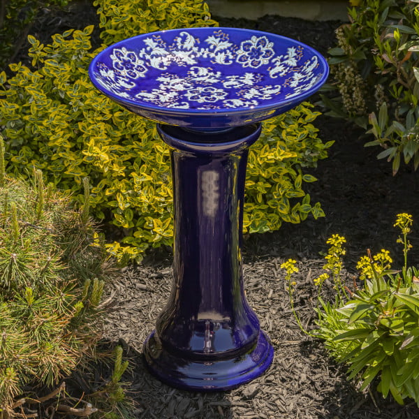 24 inch tall porcelain blue pedestal birdbath with hand painted light blue and ivory flower blossoms across the inner basin in garden