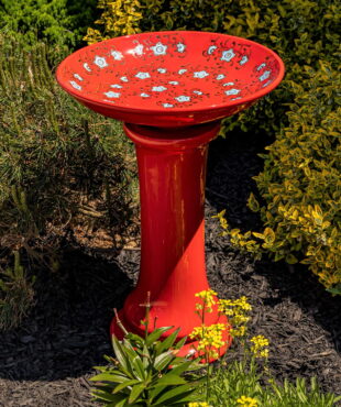 24 inch tall red porcelain pedestal birdbath with baby blue flower blossoms painted across the inner bowl in garden