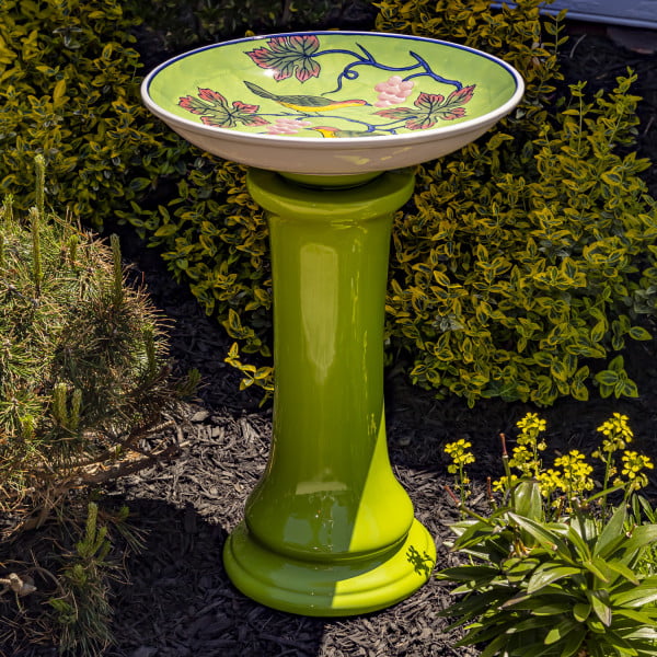 24 inch tall glossy green pedestal birdbath with painted two love birds sitting on grape vines on the inner side of the basin in garden