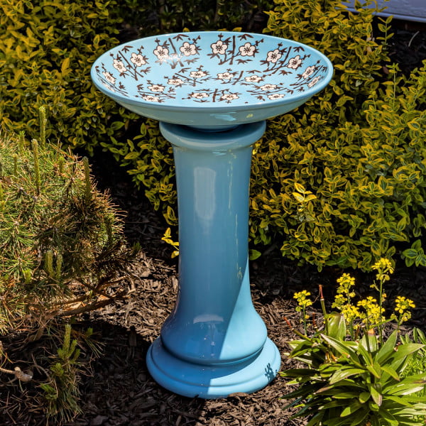 24 inch tall glossy baby blue porcelain pedestal birdbath with painted cherry blossoms on the inner basin in garden