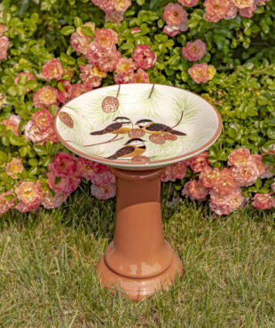 15″ Tall Round Porcelain Pedestal Birdbath with Hand Painted Birds in a Pine Tree “Finch” in front of rose bush