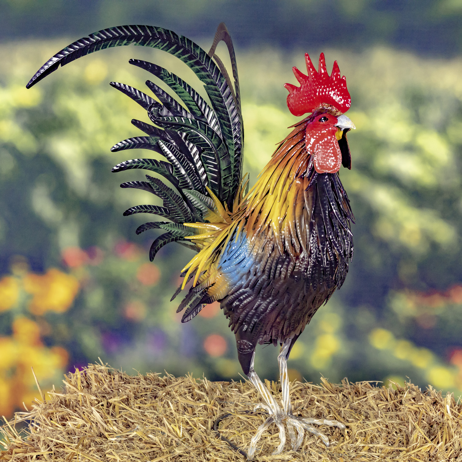 Tall painted iron Rooster figurine with bright red comb on his head, dark green and black feathers behind him while he is standing with one of his feet slightly of the hay