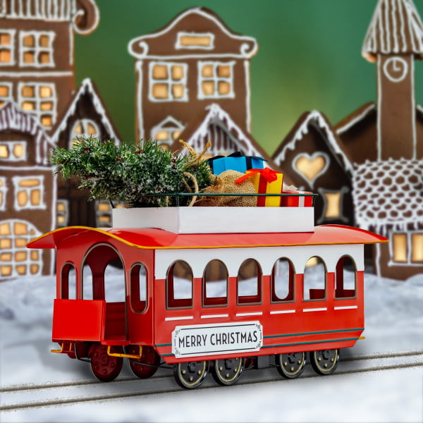 Full Length Image of 20 inch Long Vintage Style Metal Christmas Trolley with Tree & Gifts on Roof Slightly Turned and Displayed on Tracks in Front of a Beautiful Illuminated Gingerbread Village