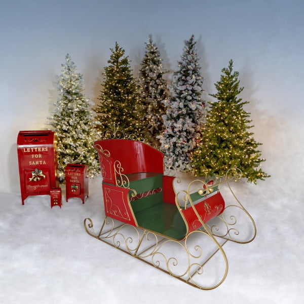 life-size classic two-seater elegant metal Christmas sleigh with a glossy red and green finish with metallic gold accents in front of mailboxes and trees