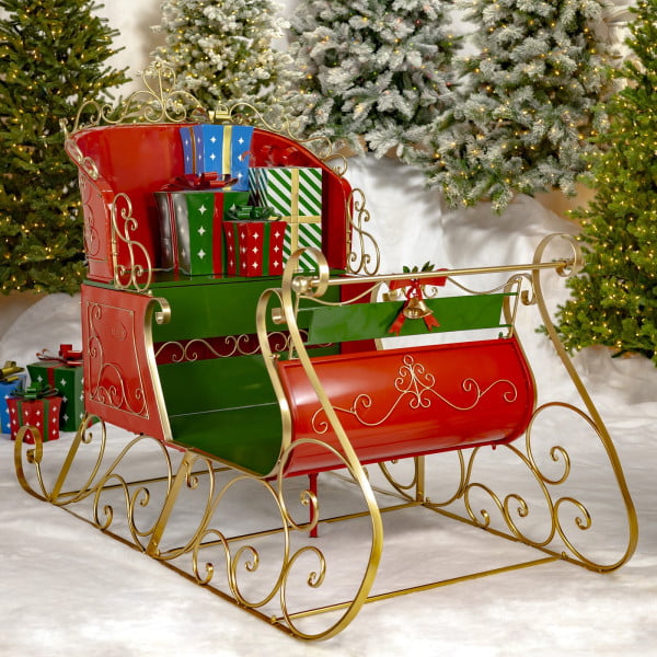 life-size classic two-seater elegant metal Christmas sleigh with a glossy red and green finish with metallic gold accents in front of mailboxes and trees and metal gift boxes on a seat