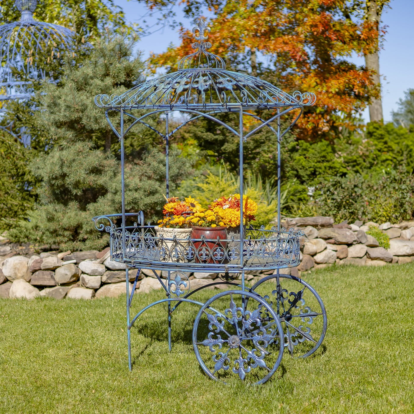 iron flower cart with two wheels and canopy roof decorated with fleur-de-lis details and flower pots standing on it hand-painted in antique blue distressed finish