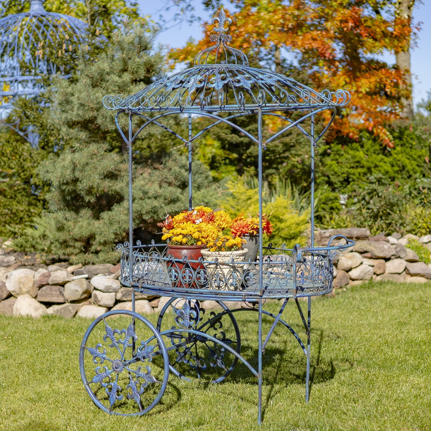 another side of iron flower cart with two wheels and canopy roof decorated with fleur-de-lis details and flower pots standing on it hand-painted in antique blue distressed finish