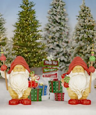 Two tall Santa gnome statues in red hats holding gifts and staffs in front of Christmas background